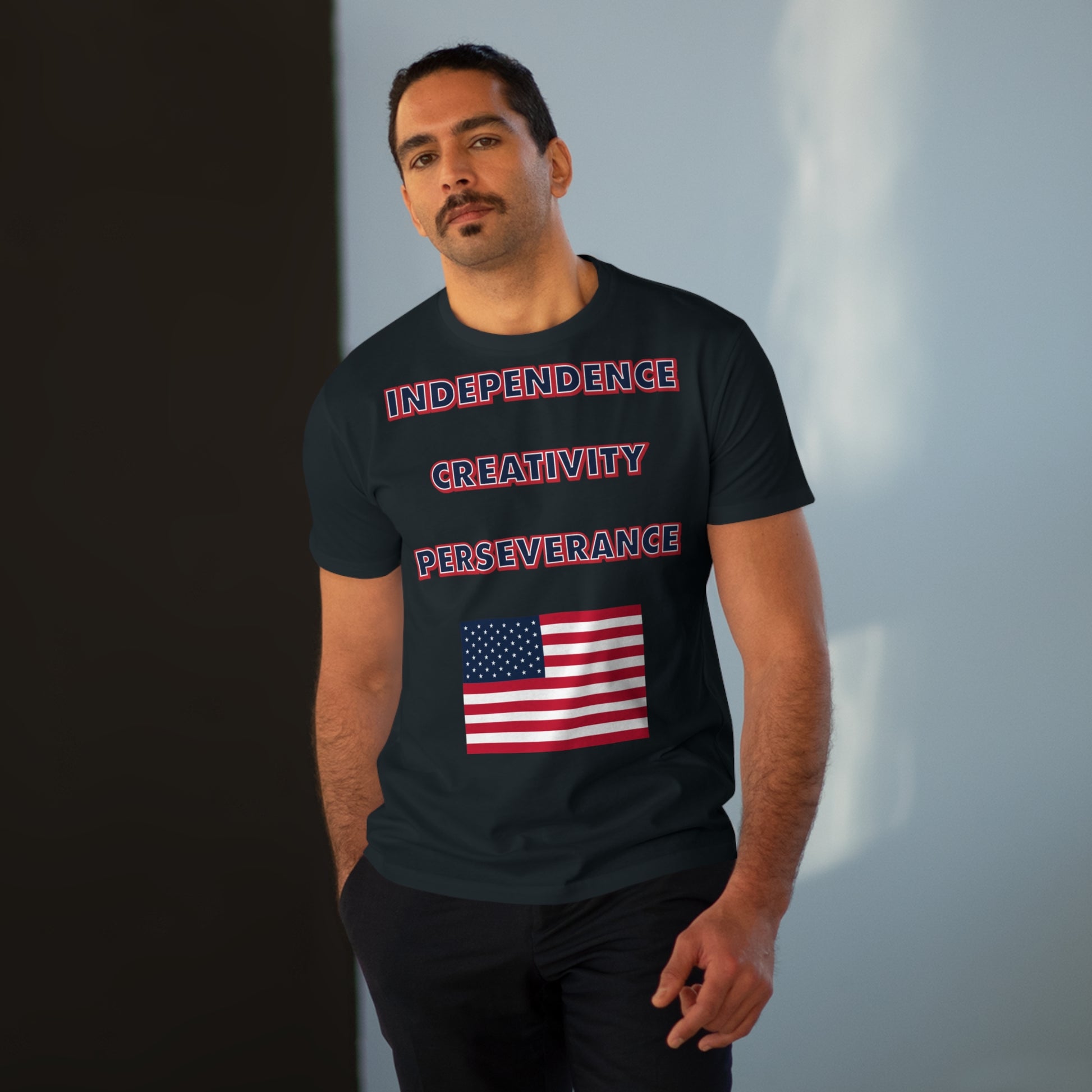 A a man with a mustache wearing a mens black t-shirt with the words independence, creativity, and perseverance written in bold, red, white, and blue letters, with an American flag located below.