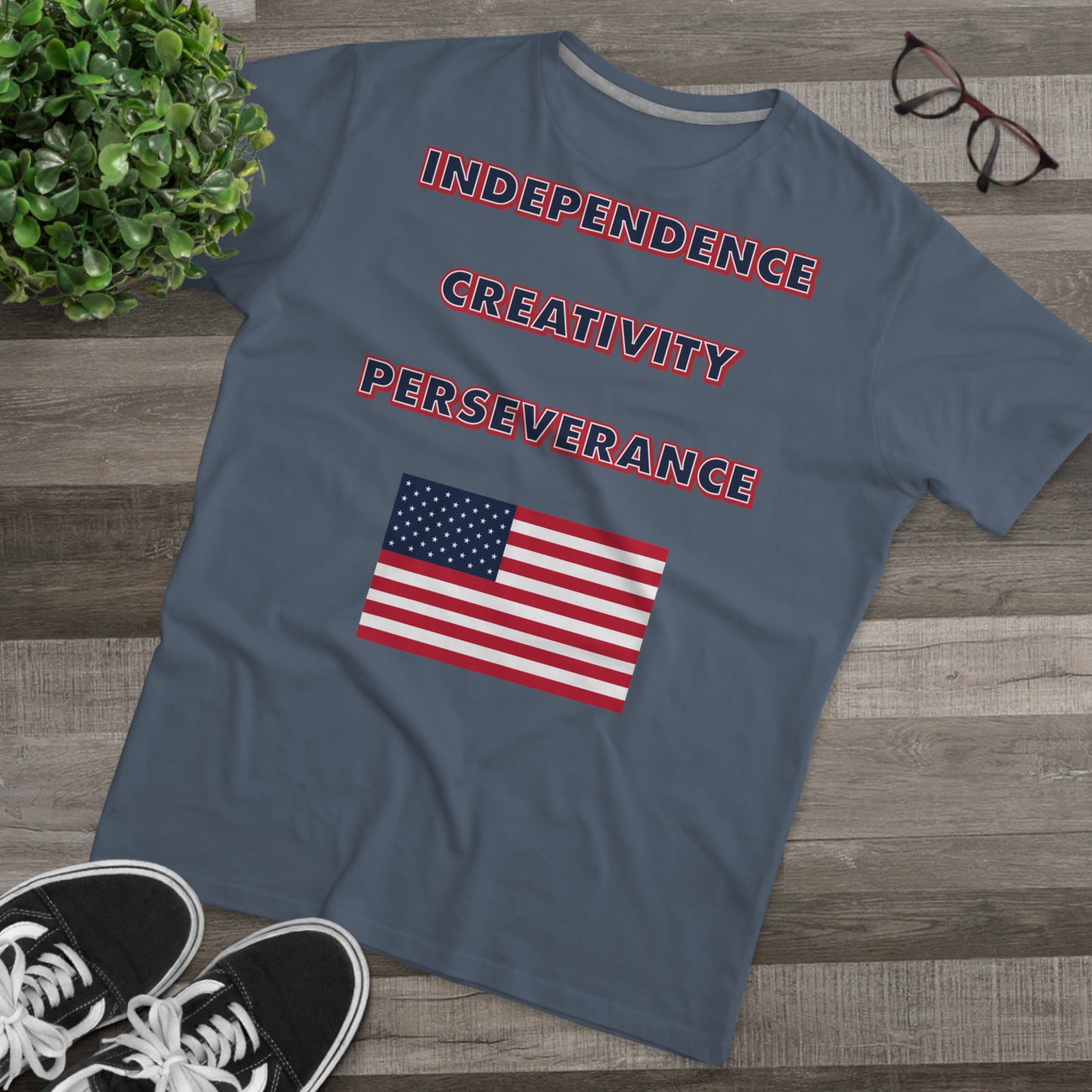 A mens grey t-shirt with the words independence, creativity, and perseverance written in bold, red, white, and blue letters, with an American flag located below.