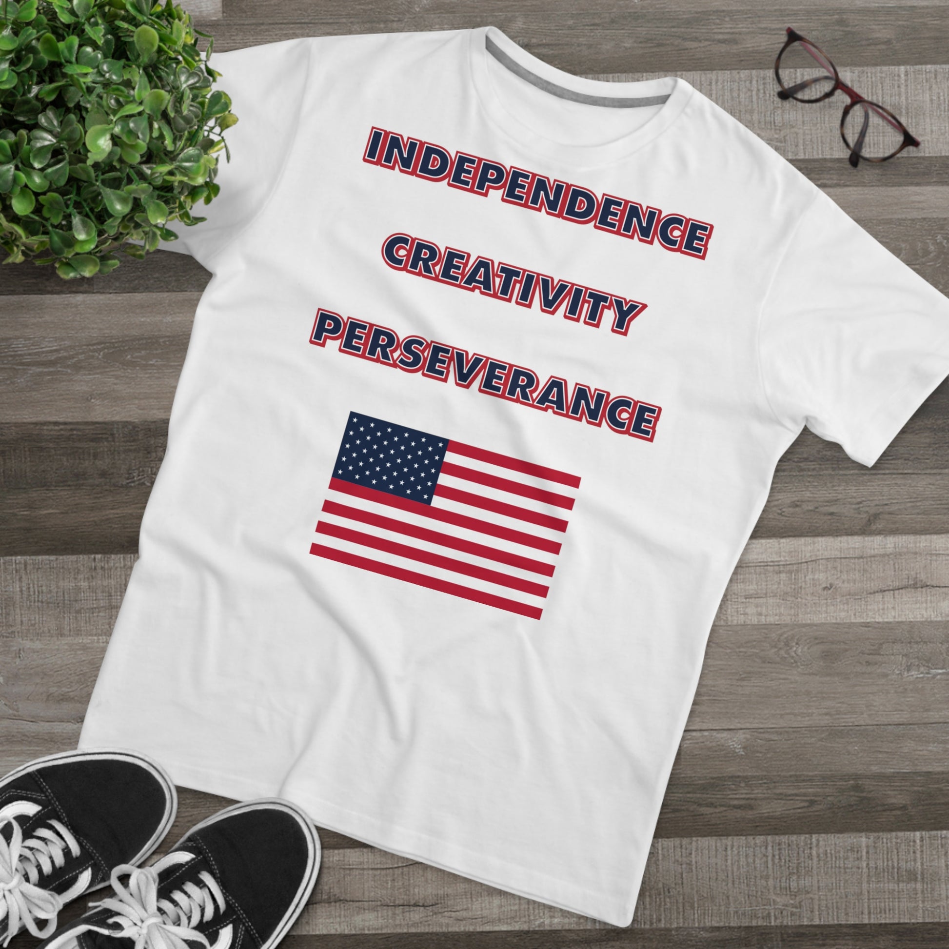 A mens white t-shirt with the words independence, creativity, and perseverance written in bold, red, white, and blue letters, with an American flag located below.