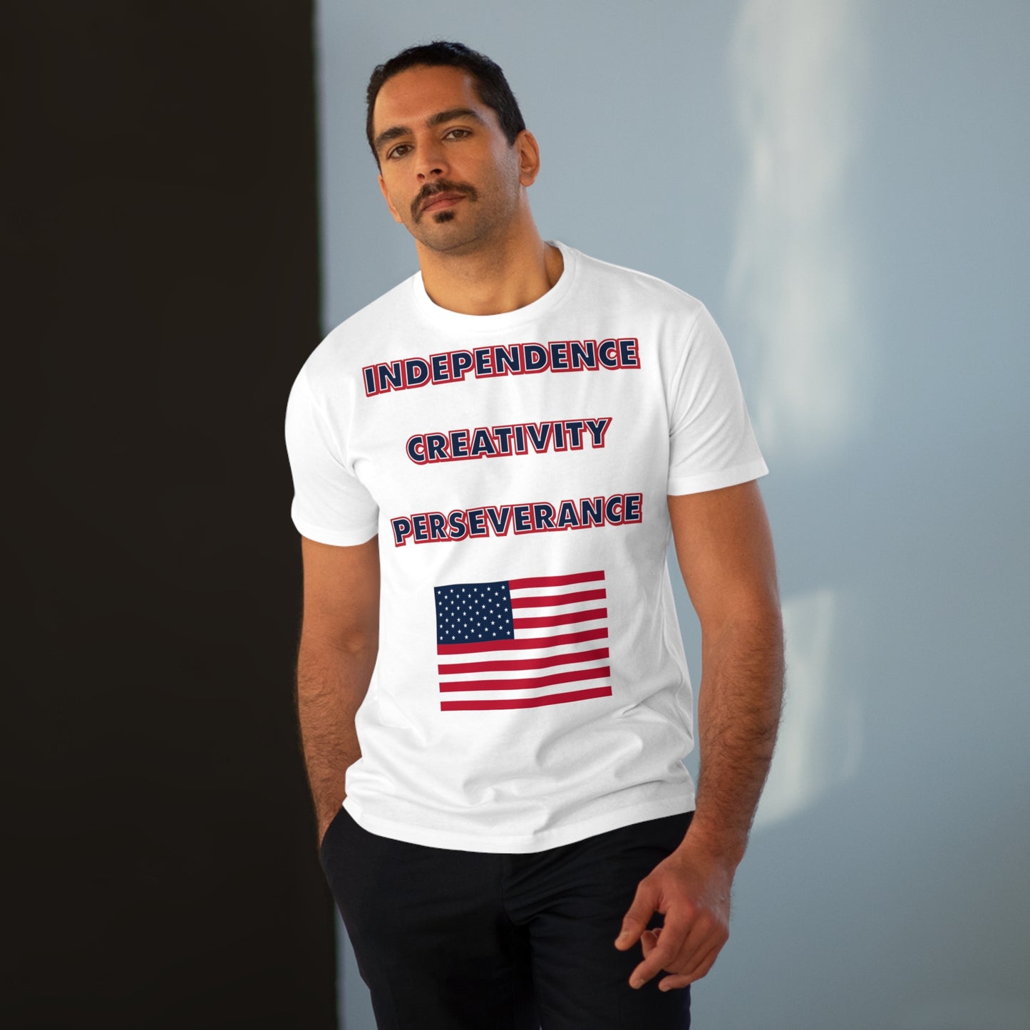 A man with a mustache wearing a mens white t-shirt with the words independence, creativity, and perseverance written in bold, red, white, and blue letters, with an American flag located below.