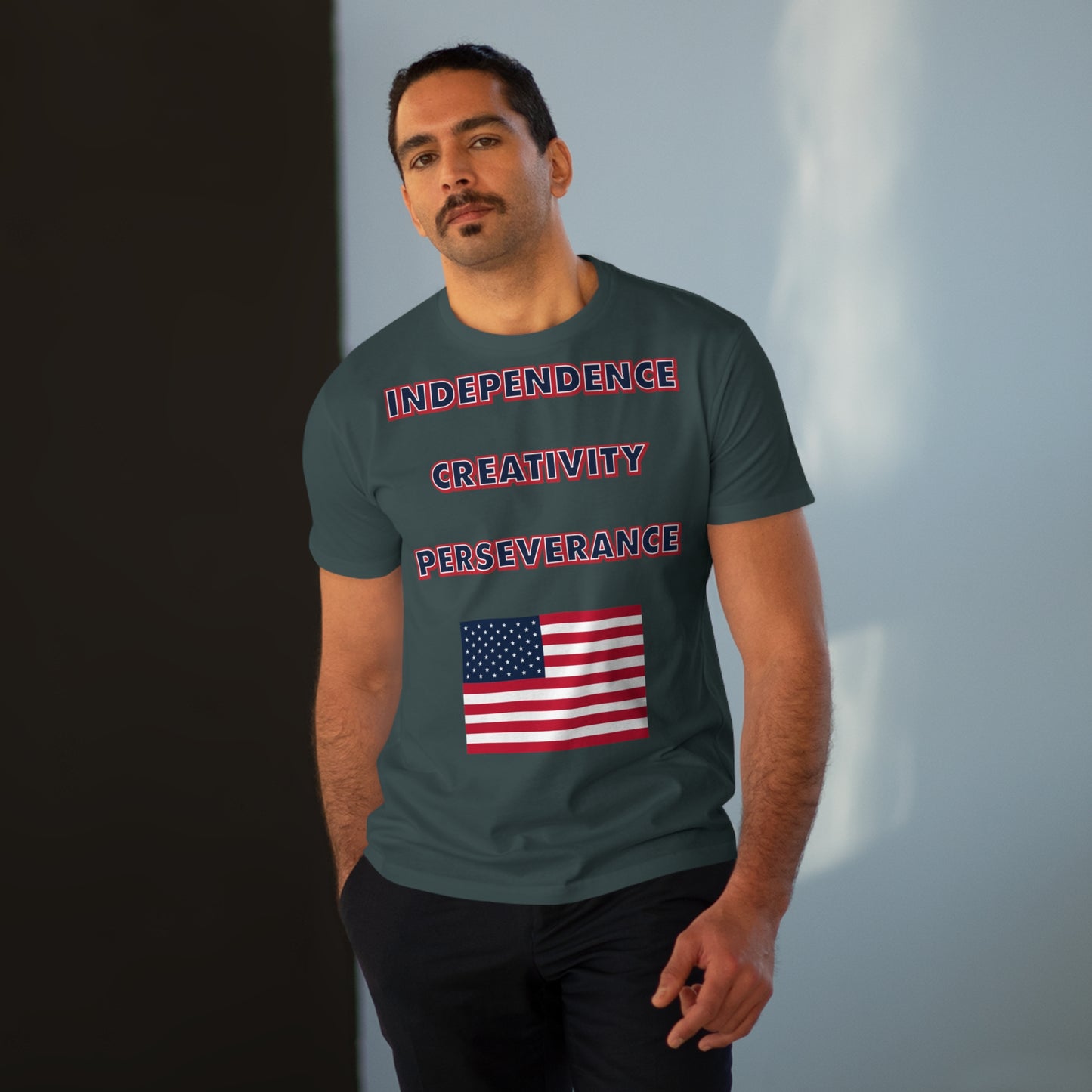 A man with a mustache wearing a mens charcoal grey t-shirt with the words independence, creativity, and perseverance written in bold, red, white, and blue letters, with an American flag located below.